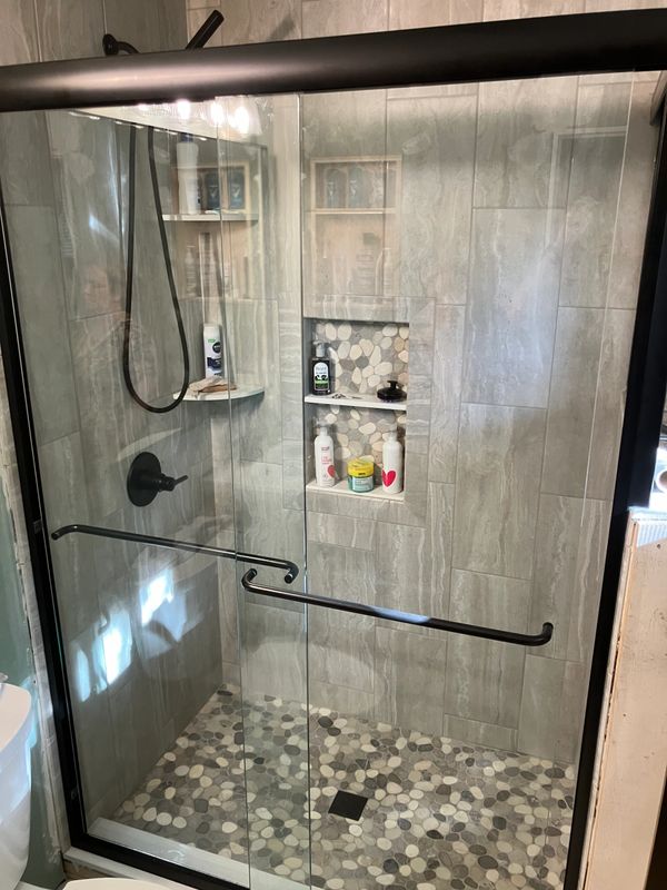 Modern shower with pebble tile floor and glass sliding door.