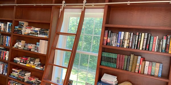 Wooden bookshelves with a rolling ladder and a window in the middle.