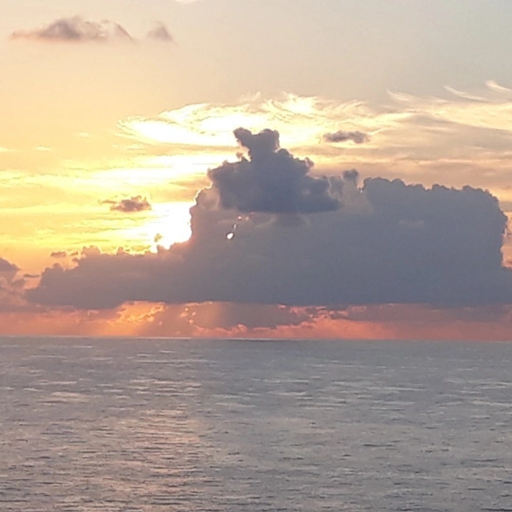Sunset over the ocean with dramatic clouds partly covering the sun.