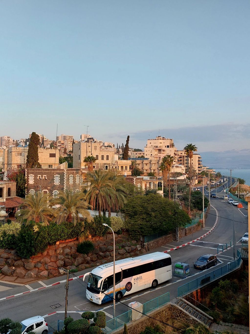 Scenic view of a coastal town with buildings, palm trees, and a bus on the road.