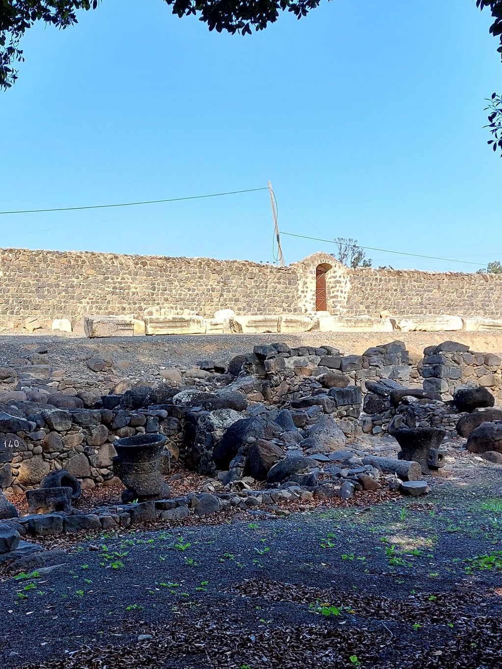 Ancient stone ruins under a clear sky with a stone wall in the background.