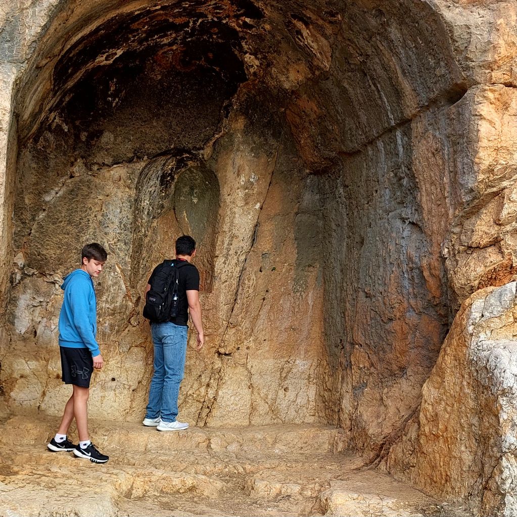 Two boys explore a rocky cave entrance with natural stone formations.