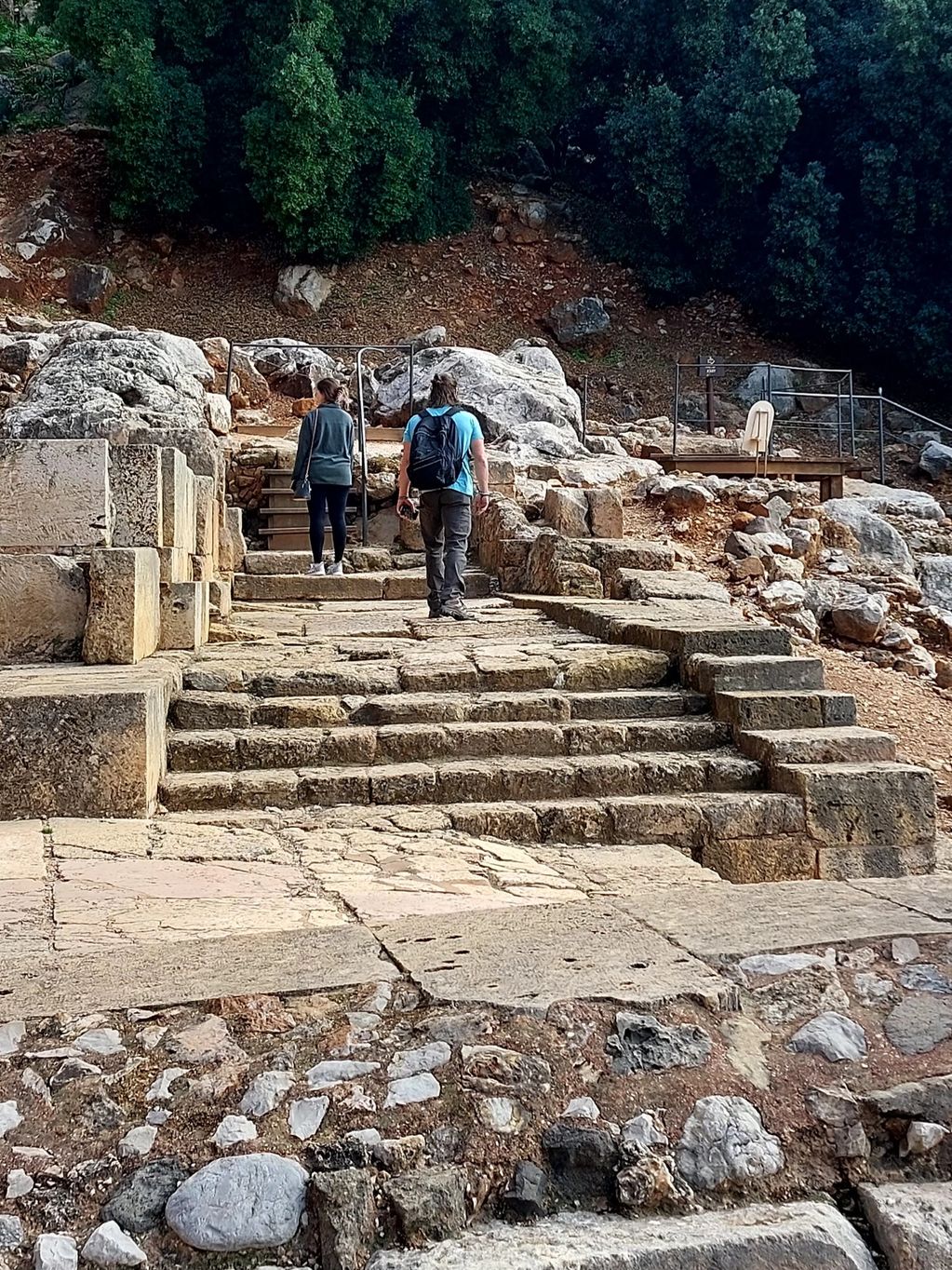 Two people exploring ancient stone ruins outdoors with greenery in the background.