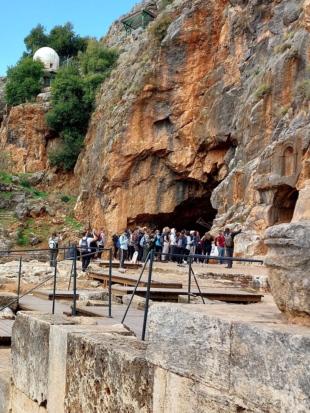 Tourists exploring an ancient cave site with stone ruins and a large column.