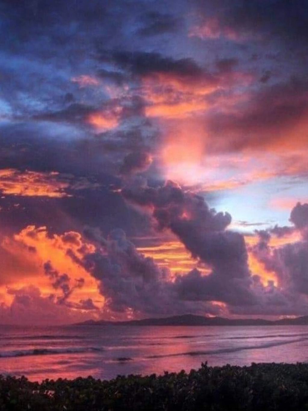 Vibrant sunset sky with dramatic clouds over a calm ocean.
