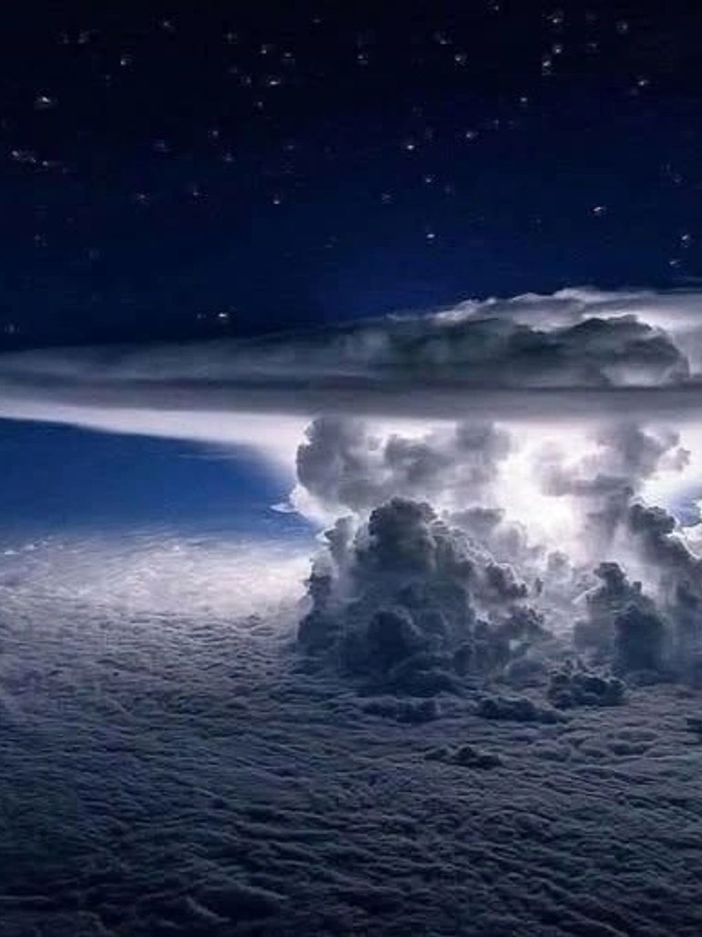 A dramatic night sky with illuminated storm clouds and stars.