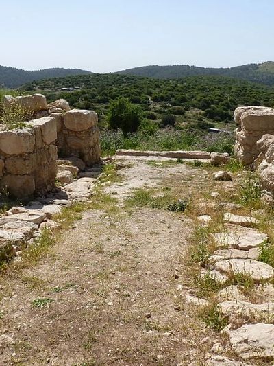 Ancient stone ruins in a natural landscape with hills in the background.