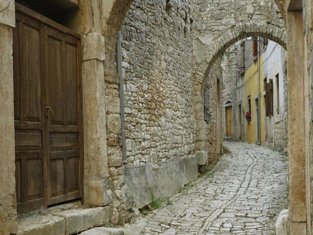 Narrow cobblestone alley with stone and yellow plaster walls and wooden doors.
