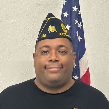 Man in a military-style cap with an American flag background.