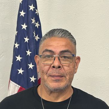Man wearing glasses standing in front of an American flag.