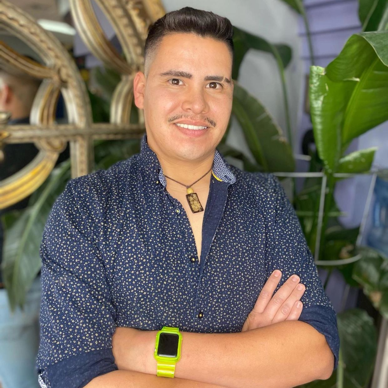 Smiling man in a patterned shirt with a green smartwatch, posing confidently indoors.