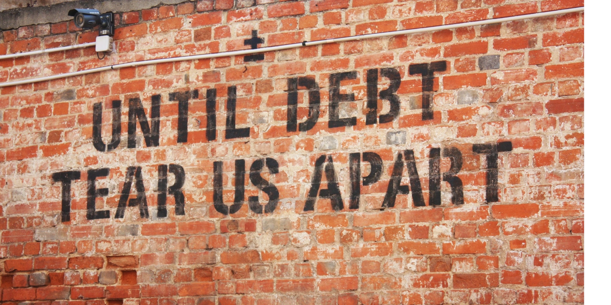 Graffiti on brick wall reads 'Until Debt Tear Us Apart'.