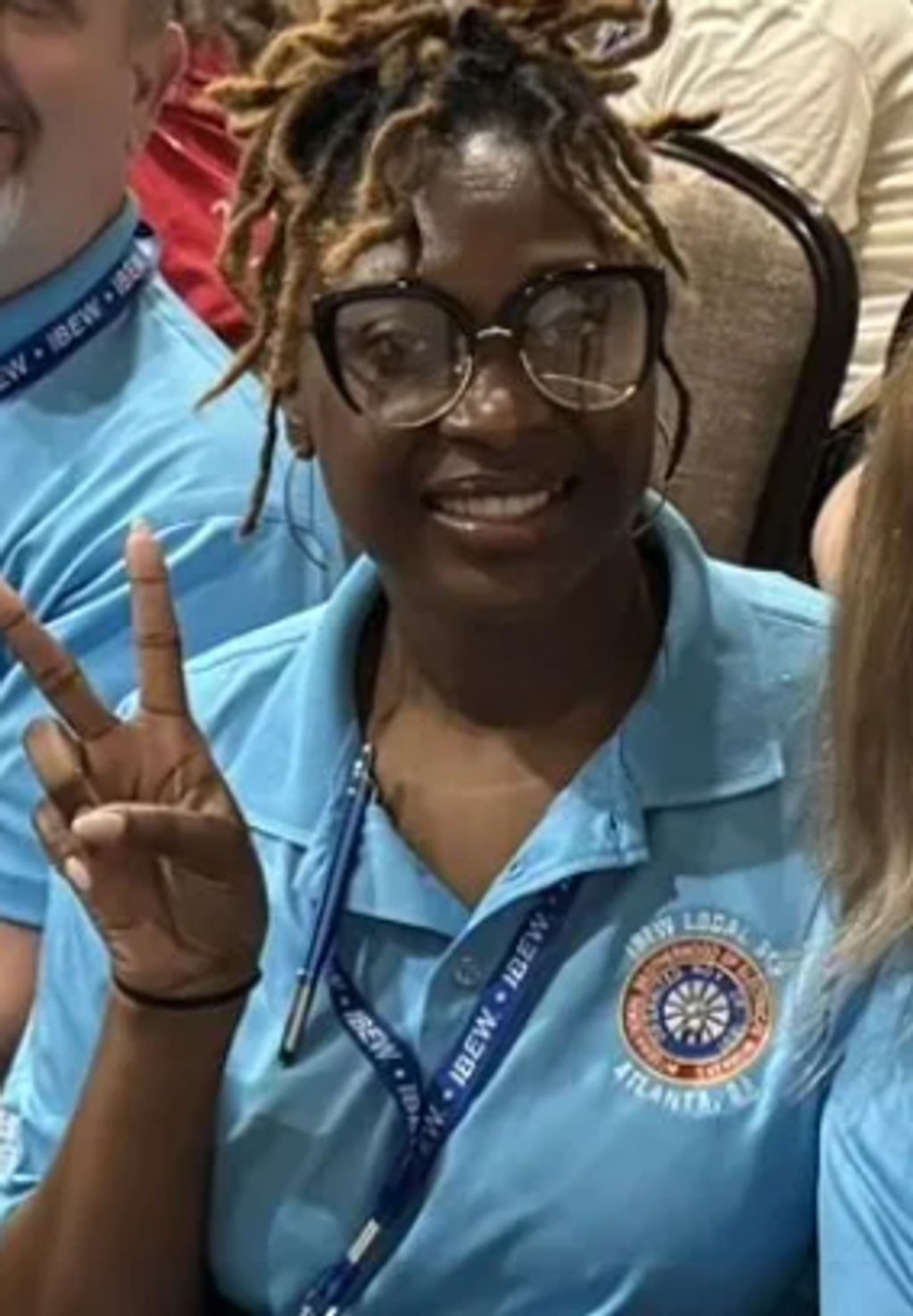Woman in blue shirt making a peace sign and smiling.
