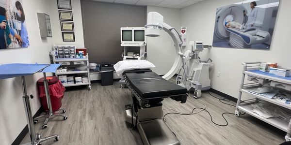 A modern medical exam room with an adjustable table and advanced imaging equipment.