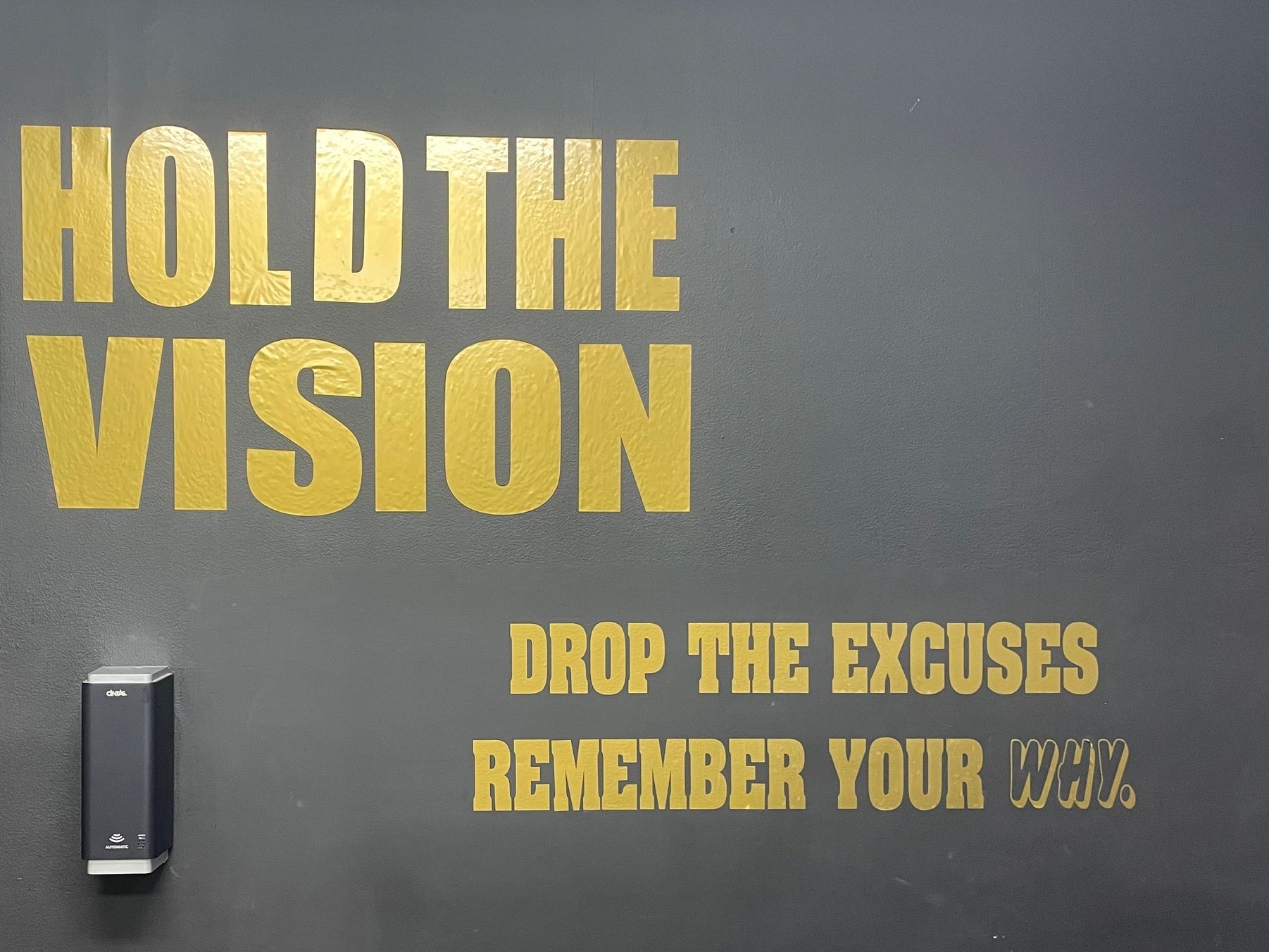 Motivational wall text in gold on gray: Hold the vision, drop the excuses, remember your why.