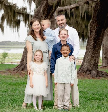 Family portrait of six people outdoors with large trees.