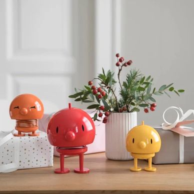 Three colorful bird-shaped toys on a wooden table with gift boxes and a vase of berries.