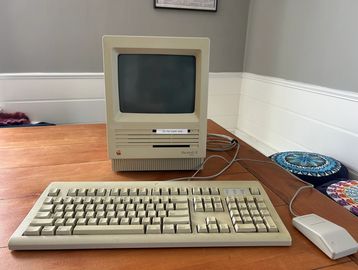 Vintage Macintosh computer with keyboard and mouse on a wooden table.