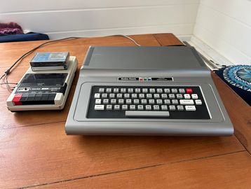 Vintage computer with cassette tape drive on a wooden table.