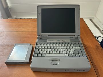 Vintage Toshiba laptop with a removable hard drive on a wooden table.