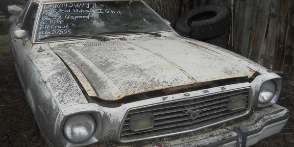 Old, rusty 1975 Ford Mustang with a dusty exterior and faded paint.