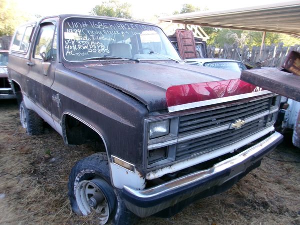 Old black Chevrolet truck with rust and flat tire in a yard.