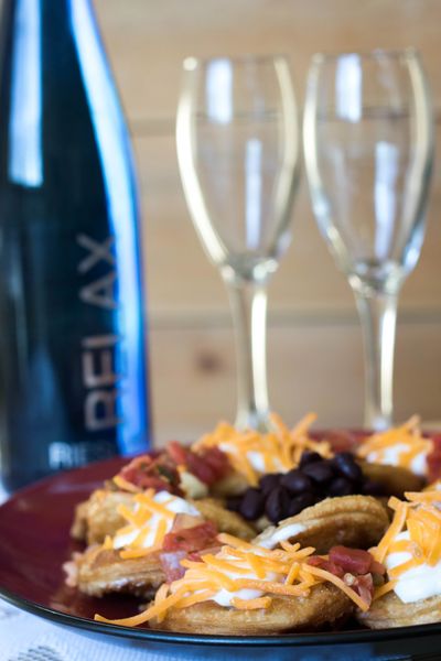 Plate of loaded nachos with shredded cheese, sour cream, and beans, with a bottle and two empty glasses in the background.