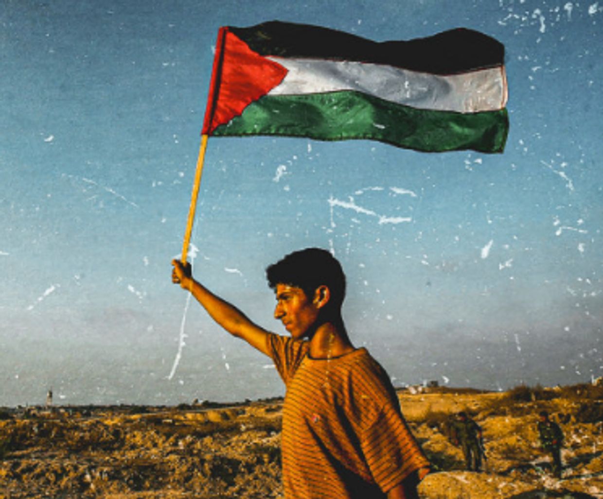 A young man holding and waving the Palestinian flag outdoors.