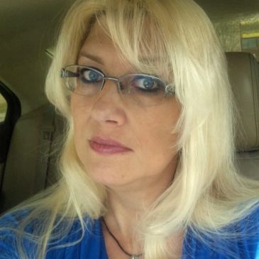 Woman with blonde hair and glasses sitting in a car.