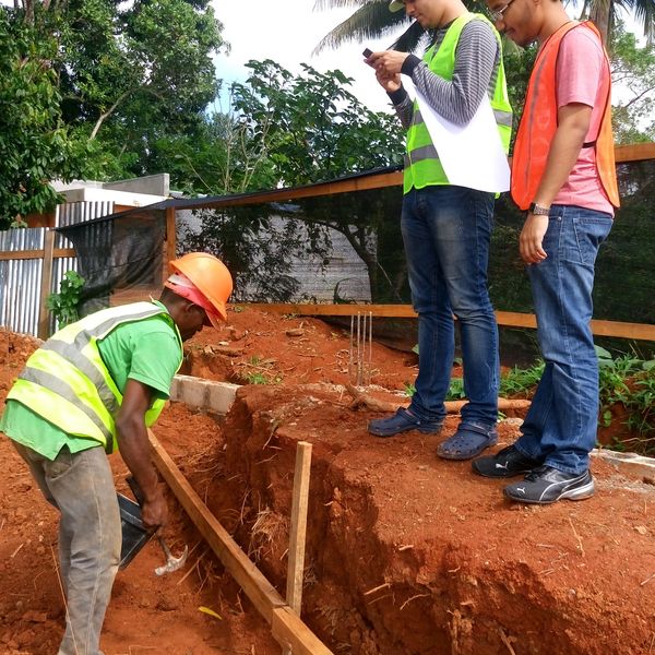 Three men at a construction site, one working and two observing.