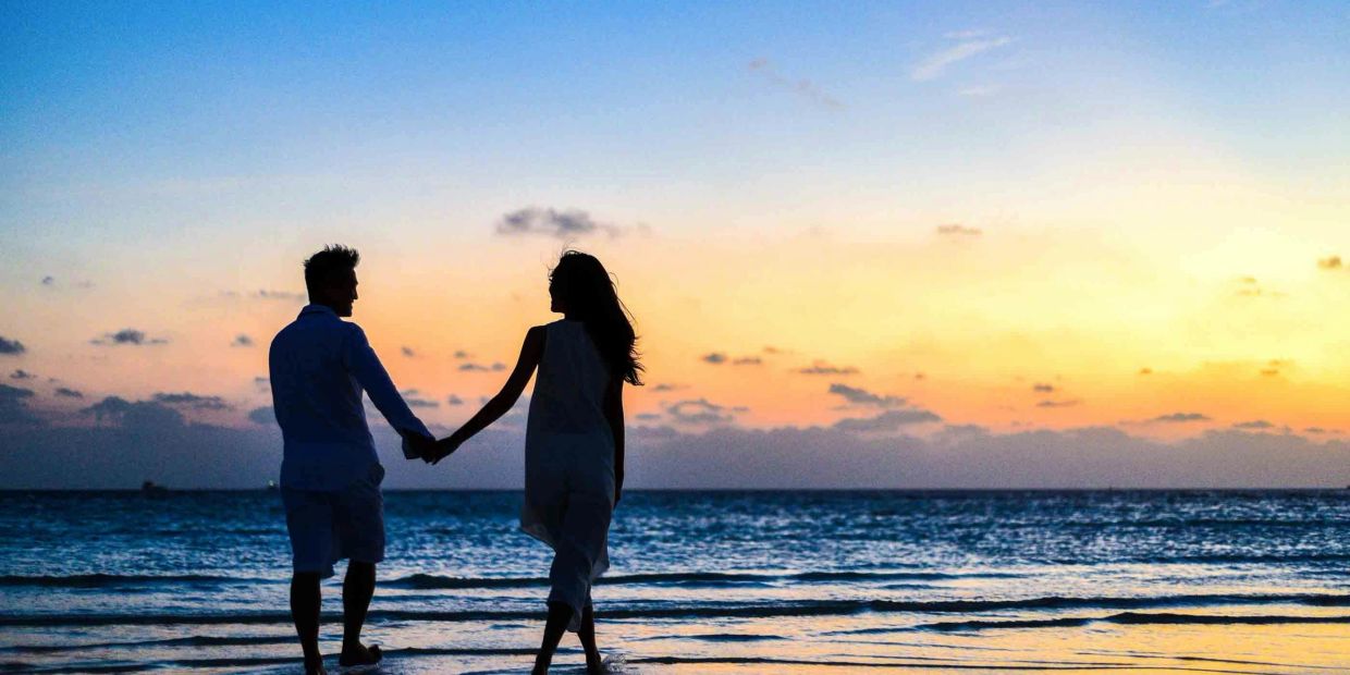 A couple holding hands walking on the beach at sunset.