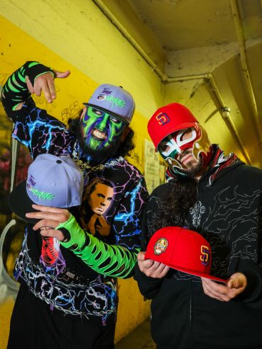 Two men with face paint and colorful hats in a urban setting.