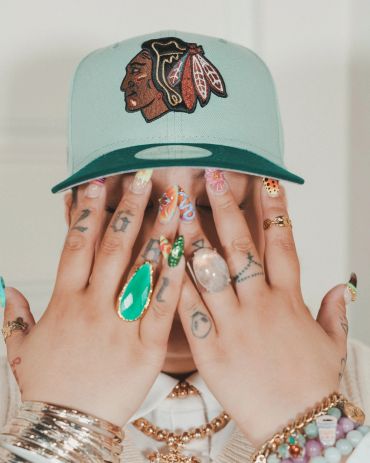 Person with colorful nails and a cap covering face.
