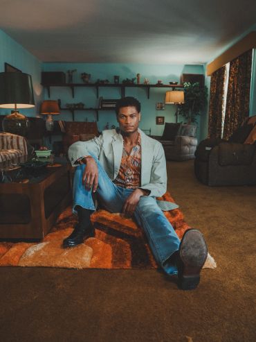 Man sitting on an orange retro rug in a living room.