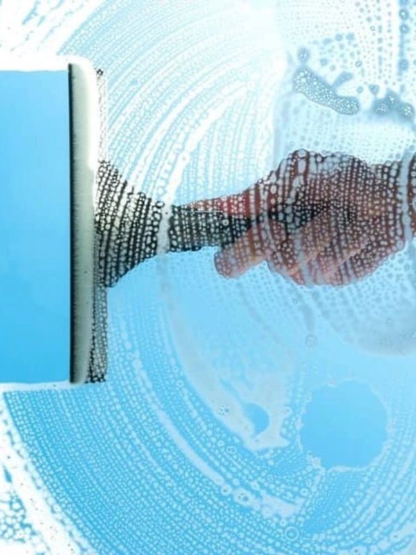 Person cleaning a window with a squeegee and soap suds.