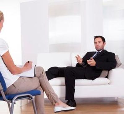 Man in a suit talking to a therapist on a couch.