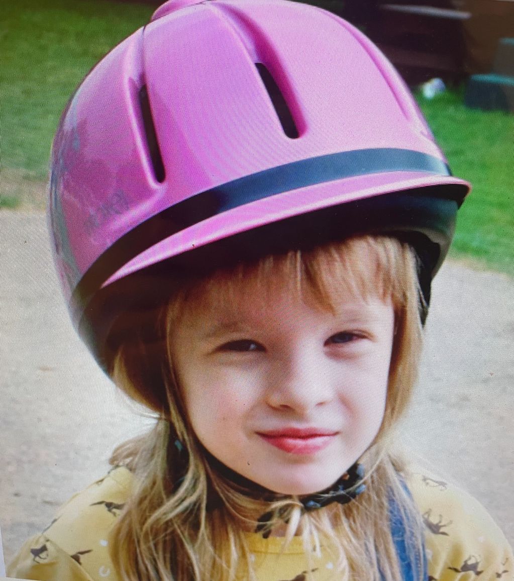 Child wearing a pink helmet and yellow shirt outdoors.