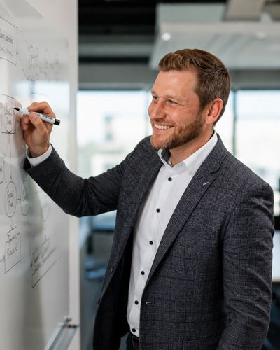 Man in business attire writing on a whiteboard and smiling.