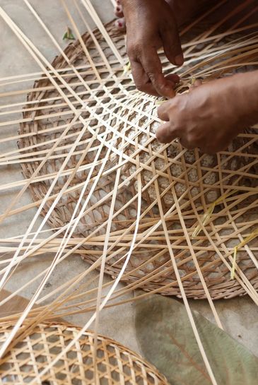 Hands weaving a basket with thin wooden strips.