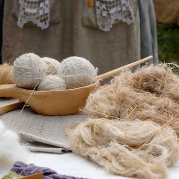 Hand-spun yarn balls and raw fiber on a wooden tray and table.