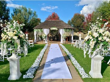Elegant outdoor wedding setup with white floral arrangements and a gazebo.