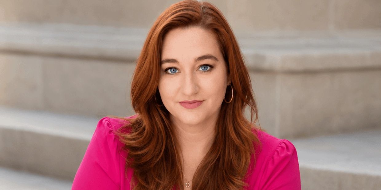 Woman with red hair and pink top smiles gently.