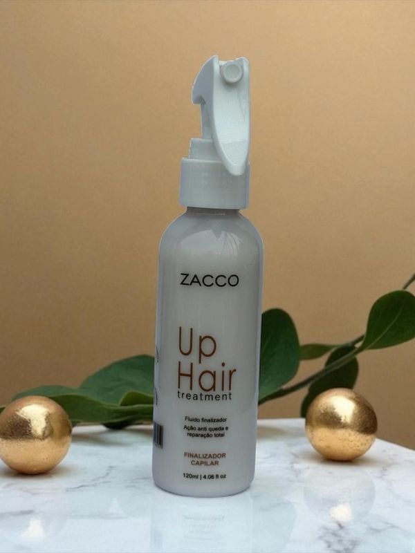 Zacco Up Hair treatment bottle on marble surface with green leaves and golden spheres.