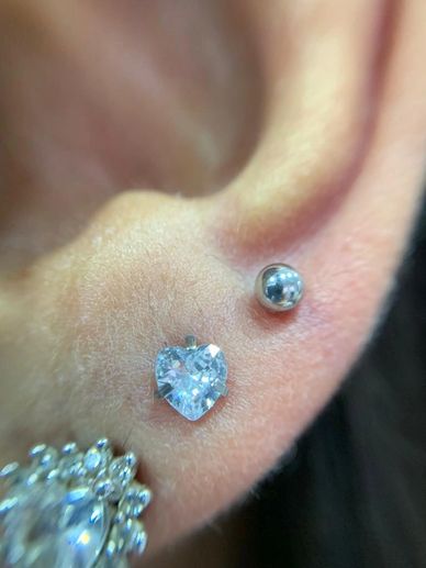Close-up of an ear with a heart-shaped crystal and a silver ball stud piercing.