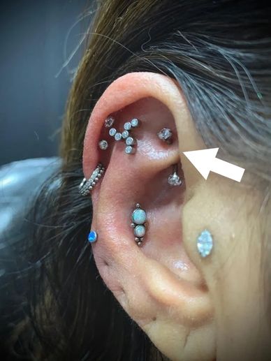 Close-up of an ear with multiple sparkling piercings and an arrow pointing to one.