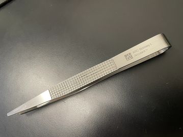 A pair of metallic tweezers with textured grip and engraved text.
