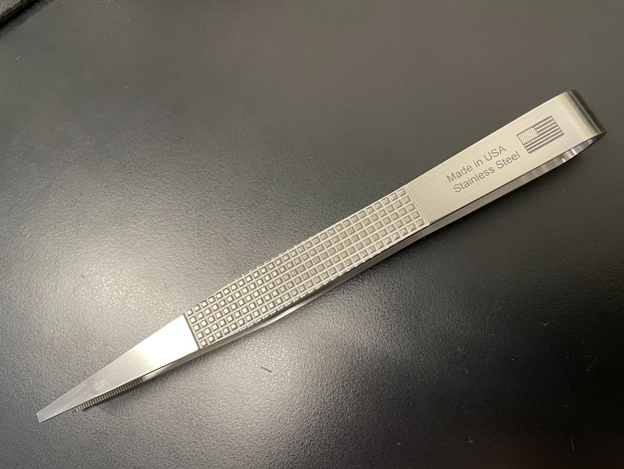 Stainless steel tweezers with a textured grip and an American flag engraving.