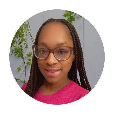 Smiling woman with braided hair and glasses in a pink sweater.