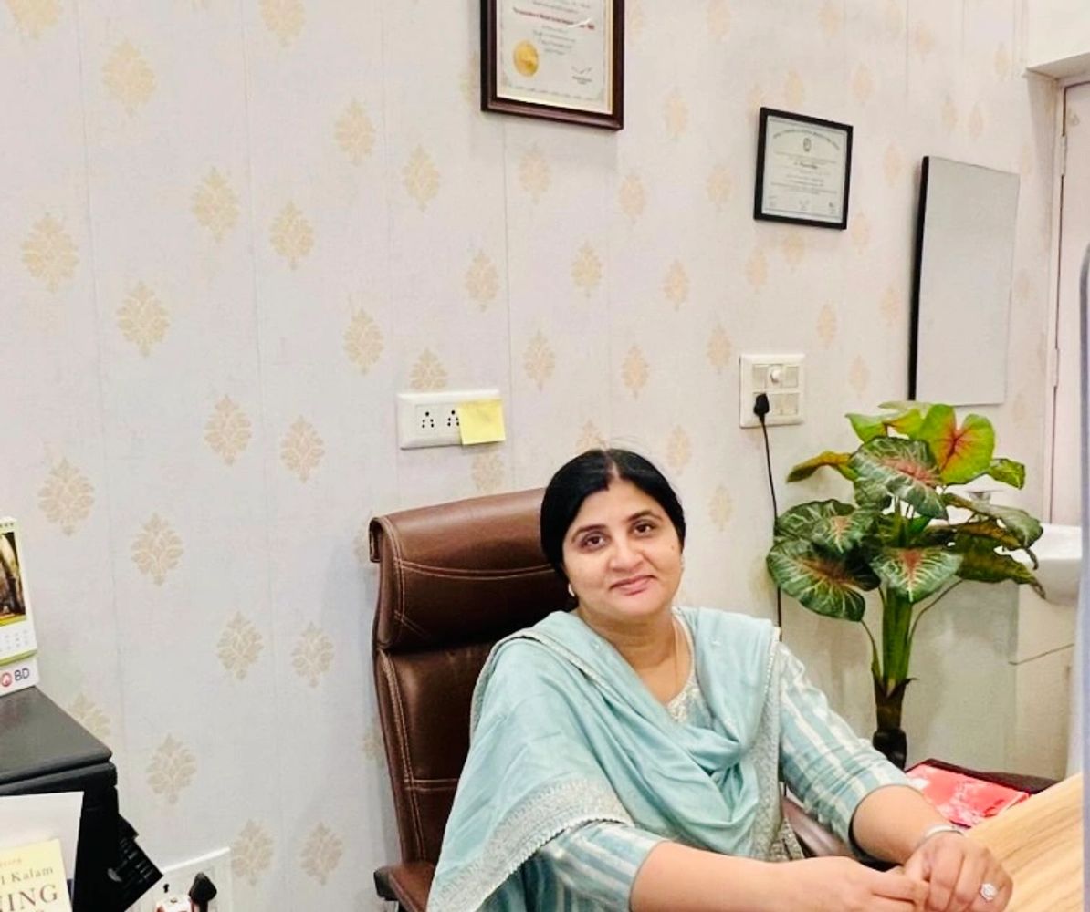 A woman in traditional attire sitting at a desk in an office with certificates on the wall.