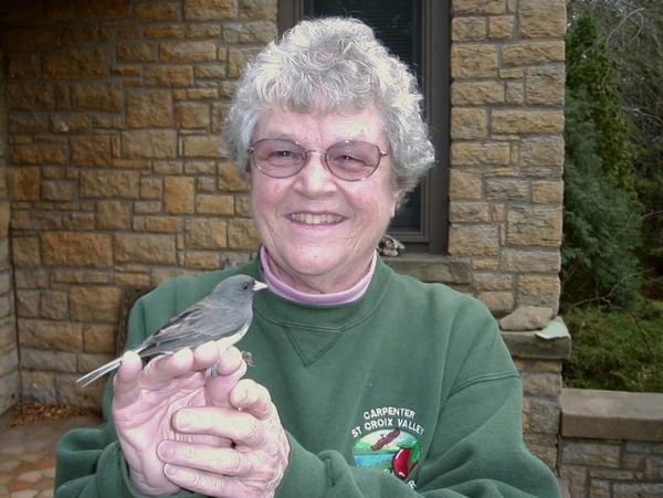 Smiling elderly woman holding a small gray bird on her hand.